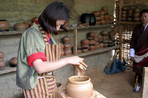 Bhutanese women making bowel with clay in greesn and brown dress