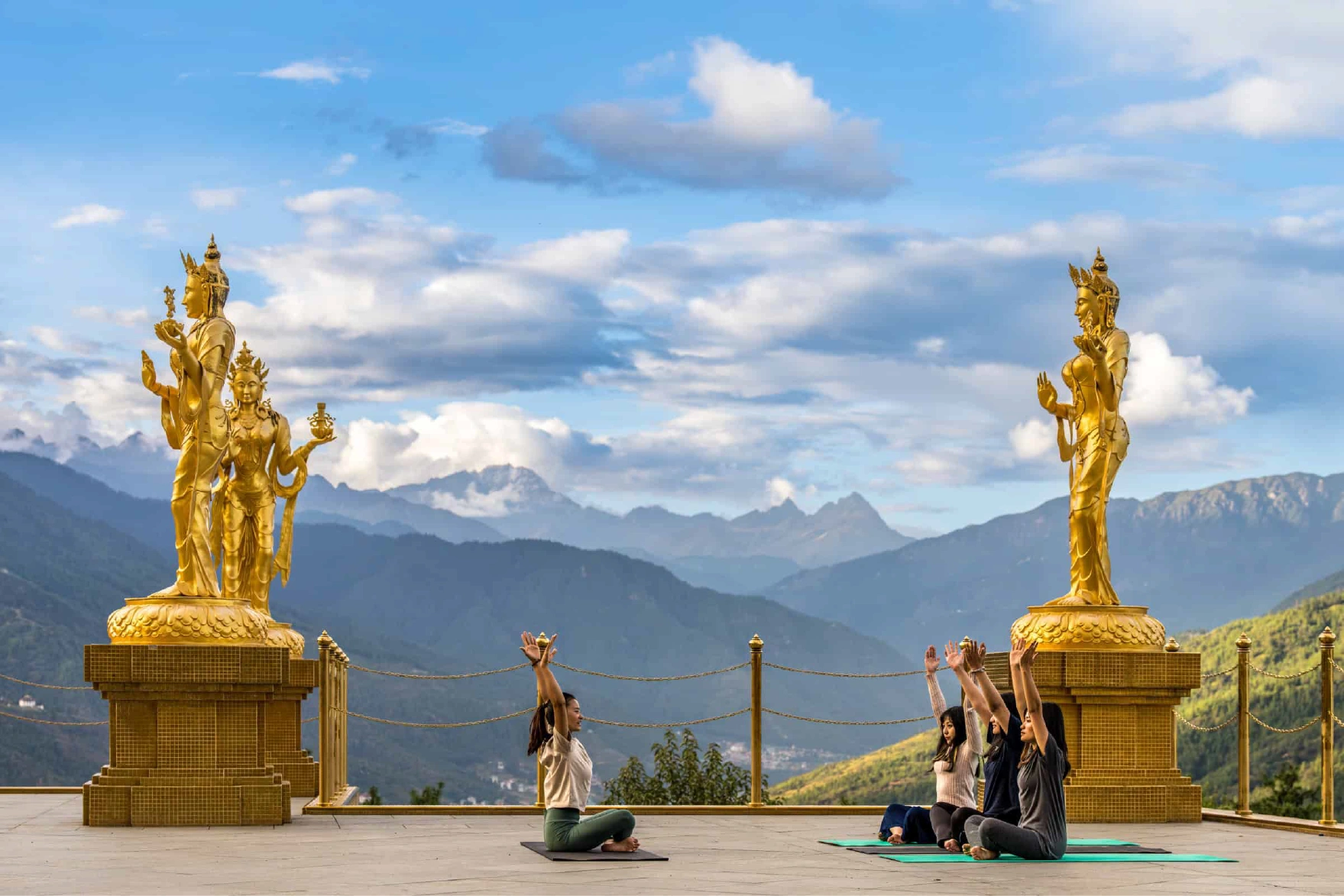People practicing yoga in front of golden Buddhist statues and Bhutanese mountains